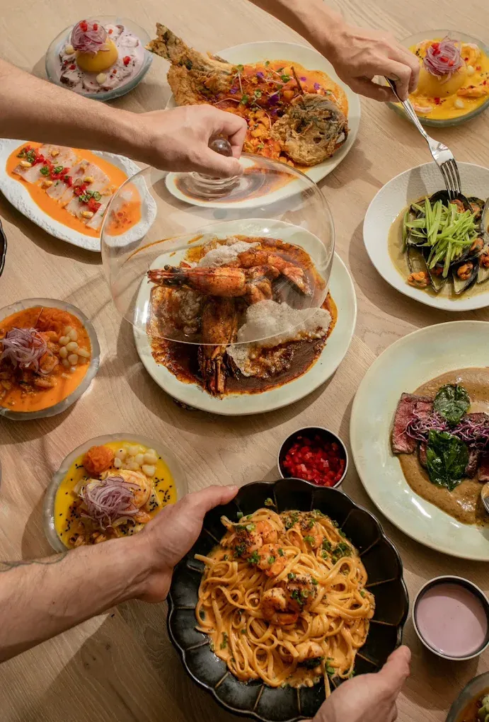 Mesa con ceviches, tiraditos, langostinos, pasta y carne servidos para compartir